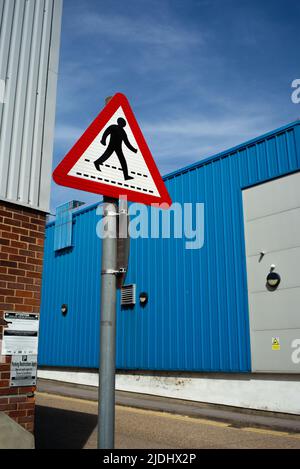 Ein rotes Warnschild für Fußgängerübergänge vor einem stark blauen Hintergrund moderner Industrieanlagen. Stockfoto