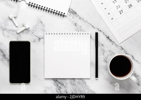 Tasse Kaffee, Telefon, Kopfhörer, Kalender und Notizbuch auf dem Marmortisch. Schwarz-weißer Hintergrund mit Kopierplatz, Nachbau. Flaches Design, pl Stockfoto