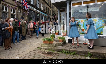 Haworth 1940 nostalgische Retro-Veranstaltung zur Lebensgeschichte (2 zwei Damen führen Live-Musik auf und unterhalten die geschäftige, überfüllte Main Street) - West Yorkshire England Großbritannien. Stockfoto