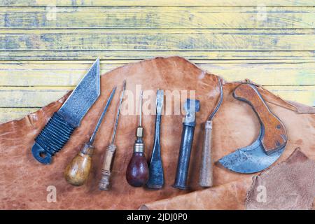 Handwerkzeuge aus Leder auf Holzhintergrund. Schreibtisch mit Lederhandwerk. Ein Teil der handgefertigten Werkzeuge auf einem Arbeitstisch Stockfoto