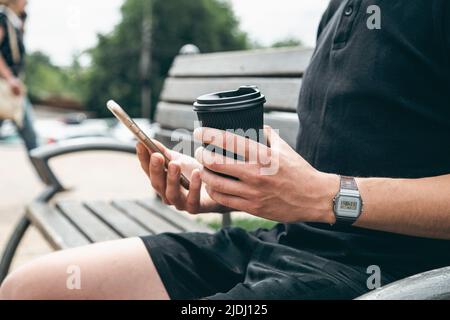 Nahaufnahme, Smartphone und ein Glas Kaffee in den Händen eines Mannes. Stockfoto