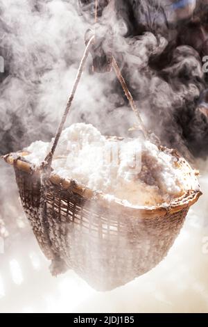 Kochendes Steinsalz auf dem Kaminofen. In Bo Kluea, Thailand, wird Salz immer noch auf traditionelle Weise hergestellt. Konzentrieren Sie sich auf den Bambuskorb mit Steinsalz. Stockfoto