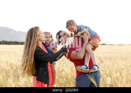 Glückliche Familie Vater der Mutter und zwei Töchter Schwestern auf der Natur bei Sonnenuntergang.sorglose Eltern Spaß mit ihren Kindern auf dem Feld. Stockfoto