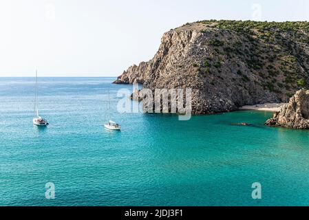 Segelboote in der fjordähnlichen Bucht von Cala Domestica mit dem Sandstrand von Cala Lunga, eingebettet zwischen felsigen Klippen im Südwesten Sardiniens Stockfoto