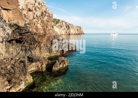 Segelboote in der fjordähnlichen Bucht von Cala Domestica mit dem Sandstrand von Cala Lunga, eingebettet zwischen felsigen Klippen im Südwesten Sardiniens Stockfoto