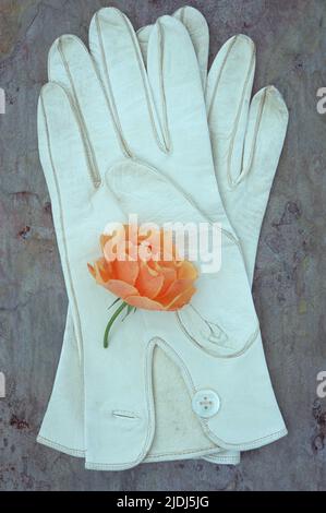 Damen-Handschuhe aus weichem, weißem Leder mit Perlmutt-Knöpfen auf Marmorstein mit blassoranger Rose Stockfoto