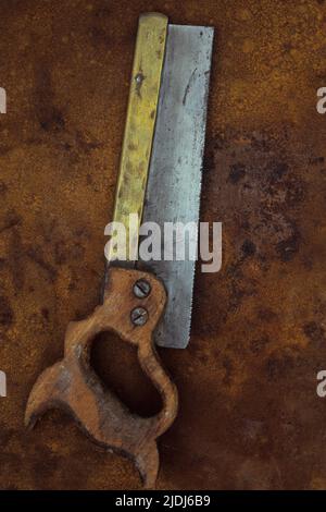 Alte, gut benutzte Zangensäge mit Holzgriff und Messingversteifung, die auf rostigen Metallblechen liegt Stockfoto