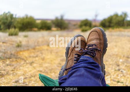 Mann, der seine Füße entspannt auf einer Fußstütze auf dem Feld ausruht. Stockfoto