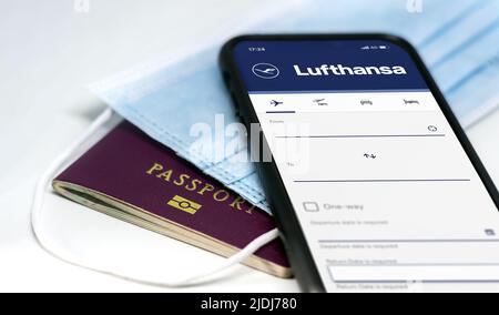 Berlin, Deutschland, MAI 2022: Telefonieren Sie mit der mobilen App der Lufthansa Airlines auf dem Bildschirm, der über einer Schutzmaske und einem Reisepass liegt. Reisesicherheit und Restr Stockfoto