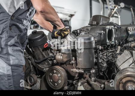 Nahaufnahme der Wartungsdienste für LKW-Motoren. Kaukasischer Mechaniker, der kleine Reparaturen macht, arbeitet mit seinem Kombinationsschlüssel an der lokalen Autowerkstatt. Stockfoto