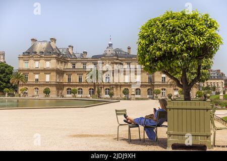 PARIS, FRANKREICH - 19. JUNI 2022: Der Palast von Luxemburg im Jardin du Luxembourg an einem heißen Sommertag. Frau relxing im Schatten eines Baumes. Stockfoto