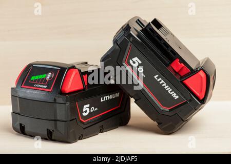 Lithium-Akku für Akku-Bohrmaschine. Schrauberbatterie. Vier Batterien mit Ladeanzeige liegen auf einem Holzhintergrund Stockfoto