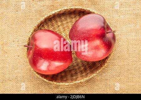 Zwei reife rote Äpfel auf Strohplatte auf Sackleinen, Nahaufnahme, Draufsicht. Stockfoto