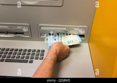 Arahal, Sevilla, Spanien. 25.Mai 2022. Detail der Hand einer älteren Frau, die Bargeld von einem Geldautomaten abheben. Einige ältere Menschen haben Schwierigkeiten, Geldautomaten zu benutzen. Stockfoto