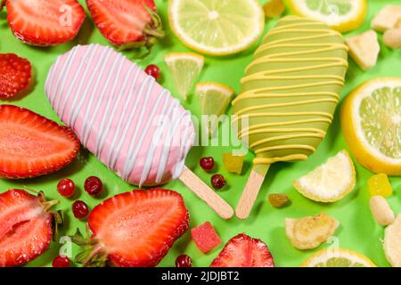Zwei Eiscremes auf einem Stock - Erdbeere und Zitrone auf grünem Hintergrund. Sommerliche Fruchtdesserts Stockfoto