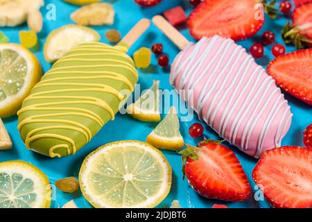 Zwei Eiscremes auf einem Stock - Erdbeere und Zitrone auf blauem Hintergrund. Sommerliche Fruchtdesserts Stockfoto