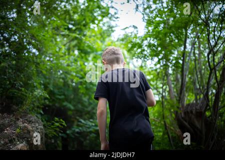 Der Junge geht vorwärts und bahnt sich seinen Weg durch den Wald Stockfoto