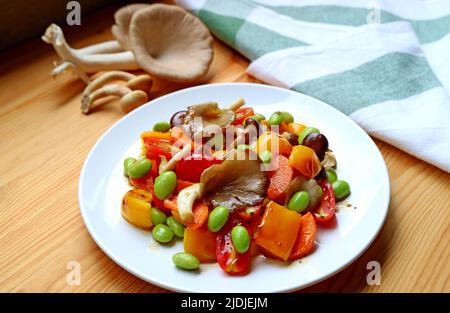 Köstlicher, farbenfroher, gegrillter Gemüsesalat mit verschwommenen frischen Pilzen der indischen Austernpilze im Hintergrund Stockfoto