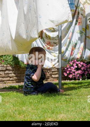 Kleinkind spielt unter der Wäscheleine im Garten, Großbritannien Stockfoto