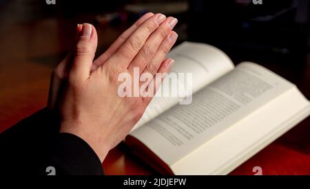 Beten Sie zu Gott, Glauben, Religion und Spiritualität Konzept. Gebet, Frau überreicht ein offenes Buch der Heiligen Bibel, Holzschreibtisch Hintergrund. Stockfoto