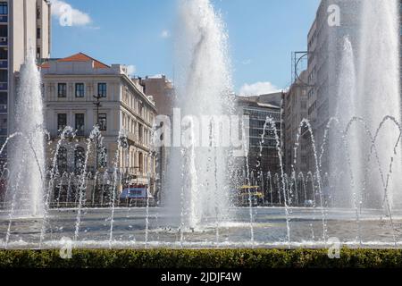 Wasserbrunnen auf dem Omonoia Platz, Athen, Griechenland. Sonniger Tag, blauer Himmel. Omonia ist ein runder platz im Stadtzentrum Stockfoto