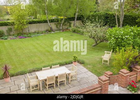 Gartenterrasse mit Gartenmöbeln auf einer Terrasse in einem von Großbritannien gestalteten Garten mit großer Liegewiese Stockfoto