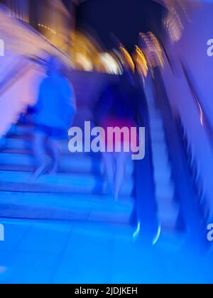 Unterführung mit einem Fußweg, bei dem Menschen den Hintergrund verwischen. Langer, leuchtender unterirdischer Tunnel und Menschen im Hintergrund. Stockfoto