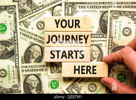 Ihre Reise beginnt hier Symbol. Konzeptwörter Ihre Reise beginnt hier auf Holzblöcken auf einem wunderschönen Hintergrund aus Dollarscheinen. Business, motiva Stockfoto