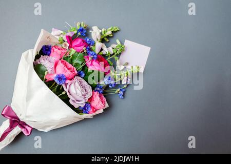 Frischer Sommerstrauß von Rosen Füchshandschuhe Junggesellenknöpfe Blumen in Papier gewickelt und auf dem Hintergrund mit Note Karte angeordnet. Geschenk für den Urlaub. Spac Stockfoto