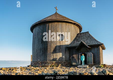 Alte Holzkirche auf dem Gipfel von Snezka, dem höchsten Berg der Tschechischen Republik, dem Riesengebirge. Mädchen in blauer Jacke zu Fuß zur Kapelle von Saint Lawre Stockfoto