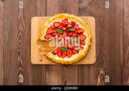 Stück Erdbeer hausgemachten Kuchen auf Holztisch.köstliche Käsekuchen mit Erdbeeren mit Minzblättern verziert.Draufsicht.gesunde Bio-Sommer Stockfoto