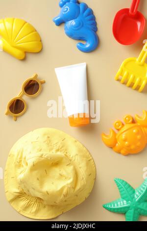 Baby Sonnenschutz cremegube mit Sandformen Spielzeug, Sonnenbrille, Hut auf beigem Hintergrund. Stockfoto