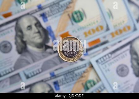 Britische 1-Pfund-Münzen aus der Nähe und verschwommene Dollar-Banknoten im Hintergrund. Konzept für Inflation. Keine Montage, echtes Foto. Stockfoto