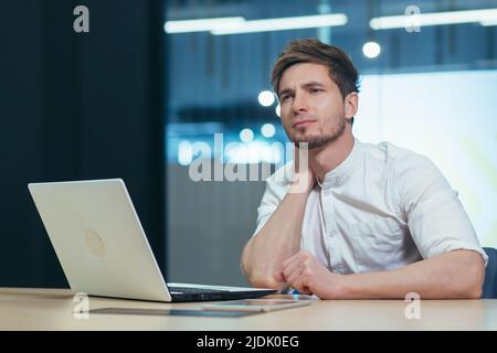 Ermüdungserscheinungen am Arbeitsplatz. Junger Mann im Büro, Freiberufler, IT-Spezialist müde, den Hals haltend, Schmerzen fühlend, Beschwerden. Braucht Ruhe Stockfoto