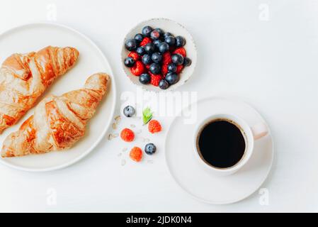 Kaffee, Croissants und Beeren Frühstück auf einem weißen Tisch. Draufsicht, flach liegend. Stockfoto