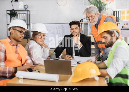 Qualifizierte Architekten, Ingenieure und Designer besprechen den Projektplan während einer wichtigen Sitzung im Büro im Detail. Geschäftstreffen des Bauteams. Konzept der Verantwortlichkeiten. Stockfoto