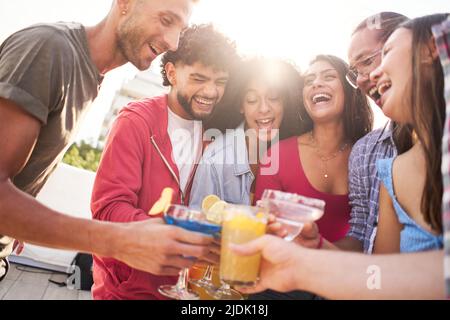 Die Gruppe der Leute amüsiert sich und lacht gemeinsam auf der Terrasse der Bar, trinkt bunte Fruchtcocktails und genießt die Freundschaft. Stockfoto