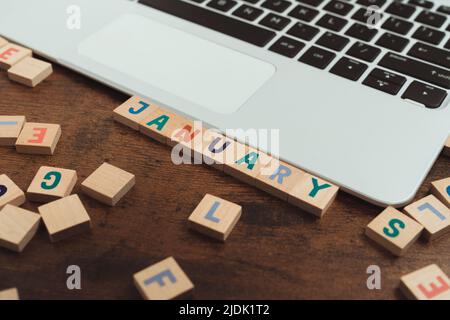 Januar. Bunte hölzerne Buchstabenrätsel, die auf einem Tisch neben dem grauen Laptop platziert sind. Werbeidee. Hochwertige Fotos Stockfoto