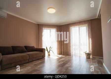 Großes, geräumiges Zimmer oder Wohnzimmer mit Sofa und großen Fenstern in minimalistischem Stil und Pastellfarben. Stockfoto