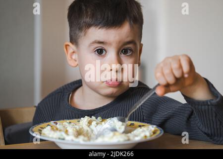 Ein sechsjähriger Junge sitzt an einem Tisch und isst am Morgen Haferflocken. Müsli zum Frühstück. Guten Morgen. Entwicklung von Kindern. Stockfoto