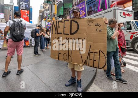 New York, USA. 21.. Juni 2022. Ein Mann zeigt ein Schild mit der Aufschrift: 'Need Money for Weed - Why Lie?' Am Times Square, neben den Teilnehmern eines kostenlosen Yoga-Kurses, um den siebten internationalen Yoga-Tag zu feiern. Kredit: Enrique Shore/Alamy Live Nachrichten Stockfoto