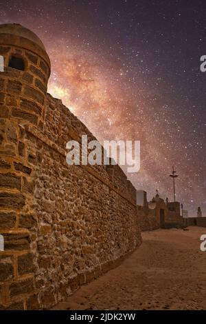 Nachtlandschaft mit der Milchstraße über den alten Steinmauern des Strandes La Caleta in Cádiz, Spanien Stockfoto