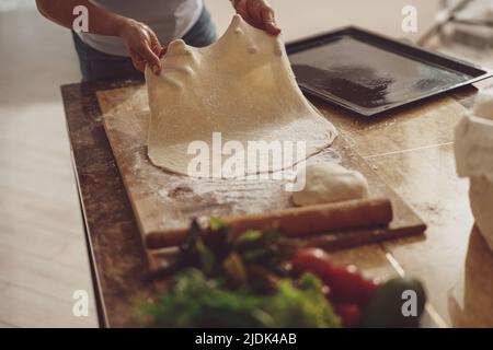 Hausfrau rollt Pizzateig auf einem Holzbrett aus, um es auf einem Backblech zu verteilen Stockfoto