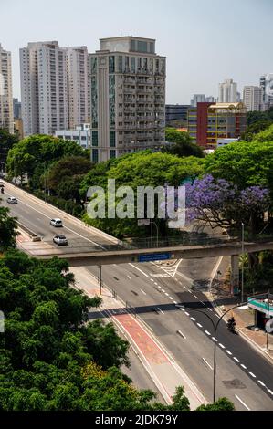 Luftaufnahme der Antarktis Avenue, die zwischen hohen Gebäuden und hohen grünen Vegetation in Agua Branca unter klarem, sonnigen blauen Himmel läuft. Stockfoto