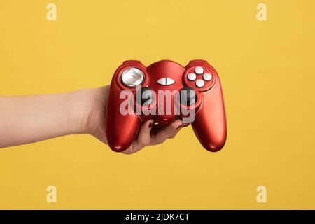 Profil Seitenansicht Nahaufnahme Porträt der Frau Hand halten zeigt roten Gamepad Joystick für das Spielen von Videospiel. Innenaufnahme des Studios isoliert auf gelbem Hintergrund. Stockfoto