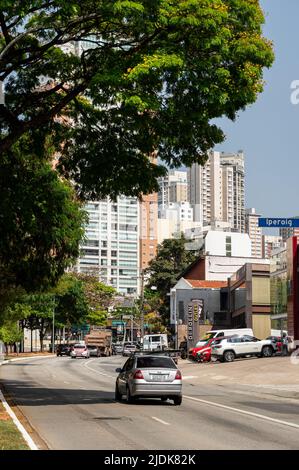 Verkehr, der an einem gekrümmten Abschnitt der Sumare Avenue in der Nähe der Iperoig Straße im Viertel Perdizes an einem normalen Arbeitstag unter sonnigem, blauem Himmel vorbeifährt. Stockfoto