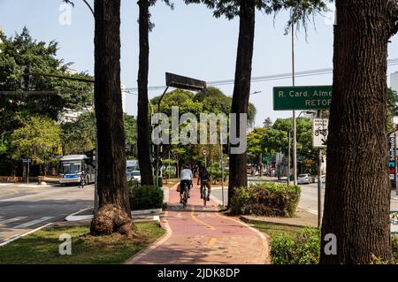 Eine Fahrradspur, die auf dem mittleren Streifen der Sumare Avenue, umgeben von grüner Vegetation, an der Kreuzung mit der Bartira Straße unter klarem blauen Himmel läuft. Stockfoto