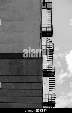 Silhouette einer Feuerflucht auf einem Hochhaus vor einem blauen Himmel mit Wolken. Einige der Treppen sind kaputt. Es ist freier Speicherplatz für Text vorhanden. Schwarz Stockfoto