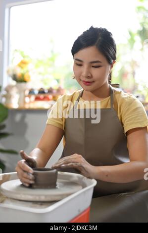 Portrait, schöne junge asiatische Frau konzentriert und konzentrierte sich auf die Herstellung einer Keramik-Tasse, Formen Ton auf einem Töpferrad in der handgefertigten Werkstatt. Stockfoto