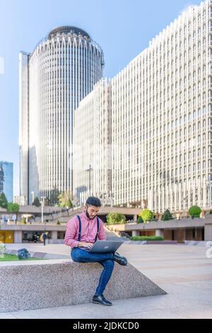 Asiatischer Mann sitzt auf einem Platz und arbeitet an einem Laptop Stockfoto